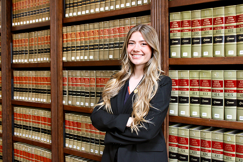 A female law student standing in a law library in front of bookshelves filled with legal volumes
